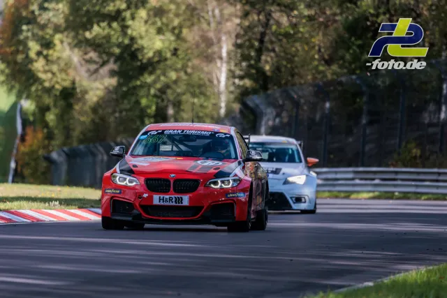Roter BMW M240i #667 führt vor weißem BMW auf der Nordschleife beim NLS-Rennen, im Hintergrund Bäume und Streckenbegrenzung.