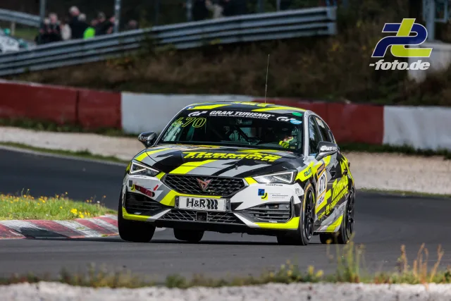Cupra Leon TCR Nummer 470 in neongelb-weiß-schwarzer Lackierung fährt über den Randstein am Nürburgring, Zuschauer im Hintergrund.