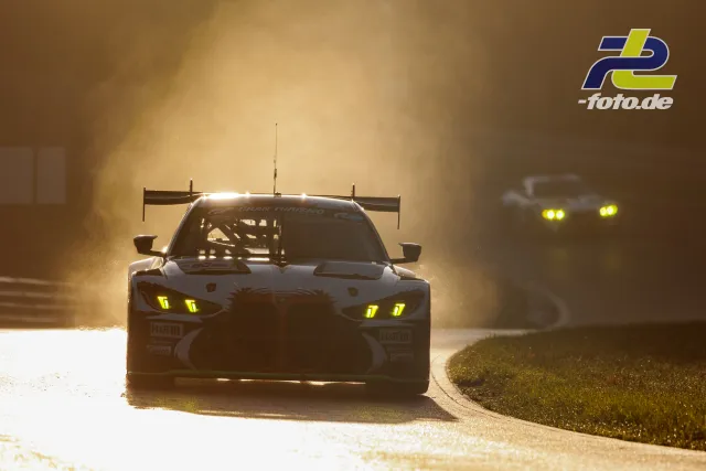 GT3-Rennwagen mit gelben Scheinwerfern im Gegenlicht bei Sonnenuntergang auf dem Nürburgring, ein zweites Fahrzeug dahinter.