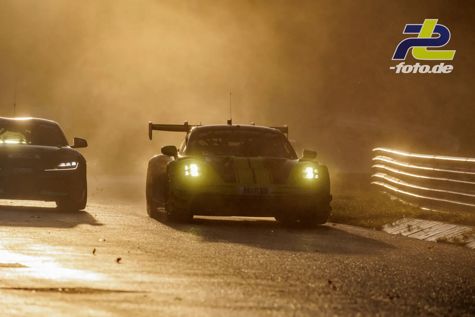 Rennwagen mit großem Heckflügel im Gegenlicht bei staubiger Atmosphäre auf der Nordschleife, weitere Fahrzeuge folgen im Hintergrund.