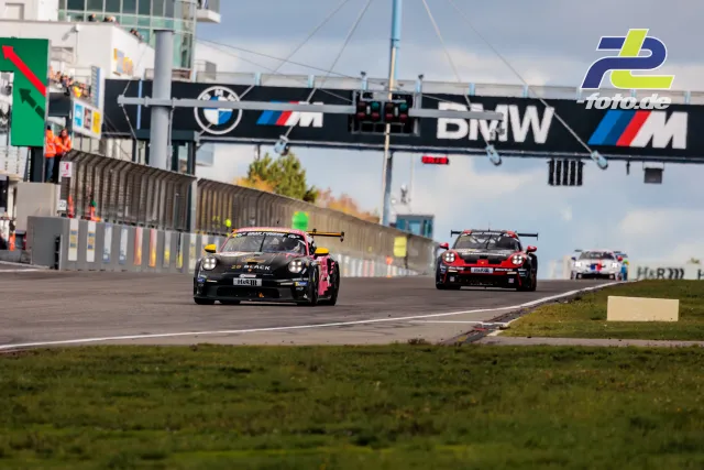 Drei Porsche-Rennwagen auf der Nordschleife beim NLS-Rennen, im Hintergrund BMW-Brücke und Boxengebäude