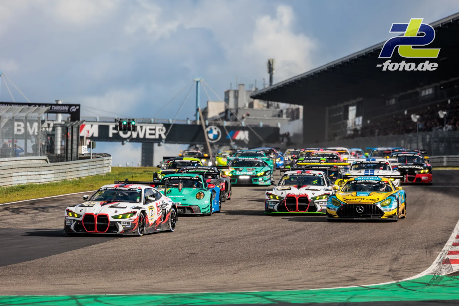 Rennstart beim NLS-Lauf am Nürburgring mit dichtem Fahrzeugfeld in der Kurve, angeführt von BMW M4 GT3, Mercedes-AMG GT3 und Porsche 911 GT3 R.