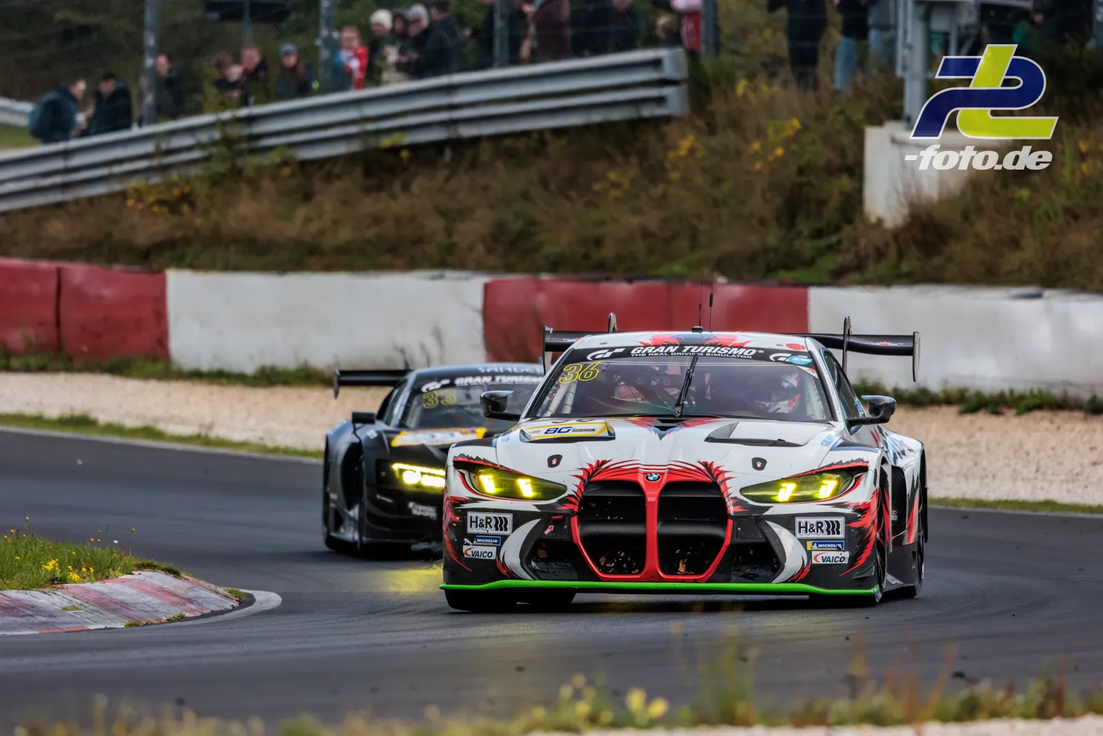 BMW M4 GT3 EVO #36 von Gamota Racing in Kurve auf dem Nürburgring, gefolgt von einem weiteren Rennwagen, während des NLS-Rennens.