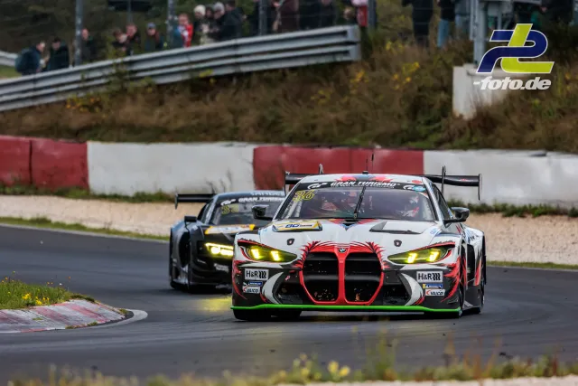 BMW M4 GT3 Nummer 36 verfolgt von zweitem Fahrzeug durch Kurve auf dem Nürburgring während NLS Rennen, Zuschauer im Hintergrund