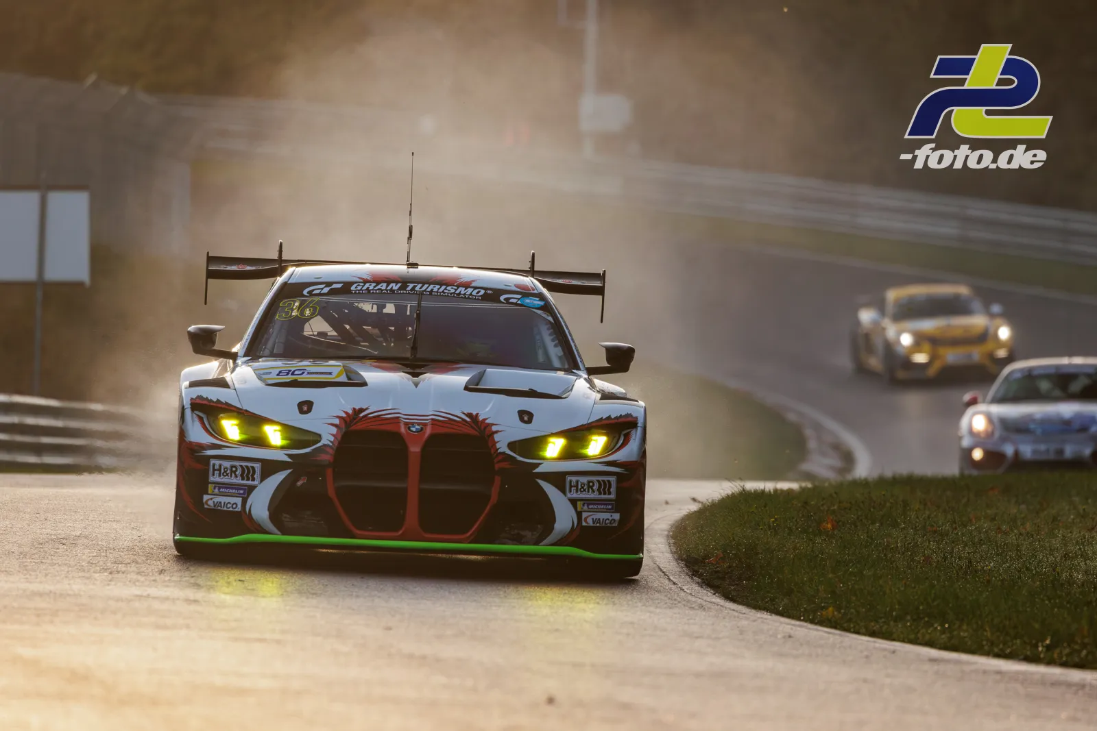 BMW M4 GT3 mit gelben Scheinwerfern in der Kurve auf dem Nürburgring im Qualifying, gefolgt von zwei weiteren Fahrzeugen.