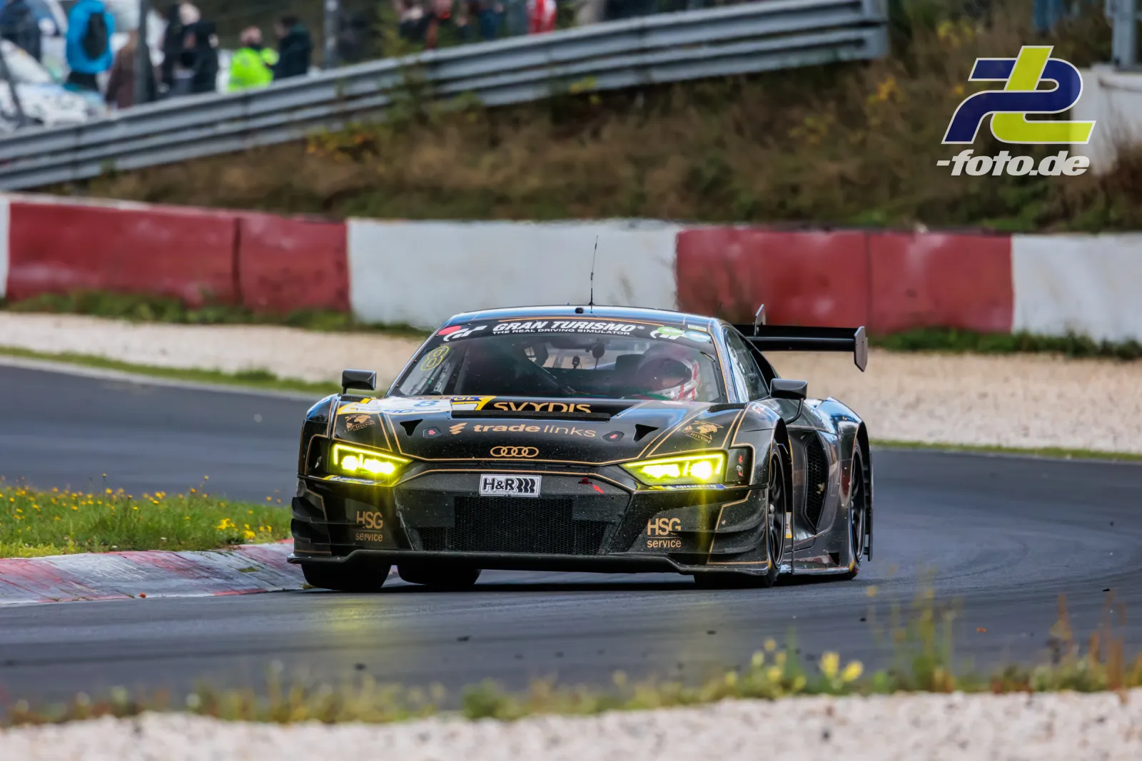 Audi R8 LMS GT3 EVO II von JUTA Racing in Kurve auf dem Nürburgring während der NLS Sportwarte-Trophy, eingeschaltete gelbe Scheinwerfer.