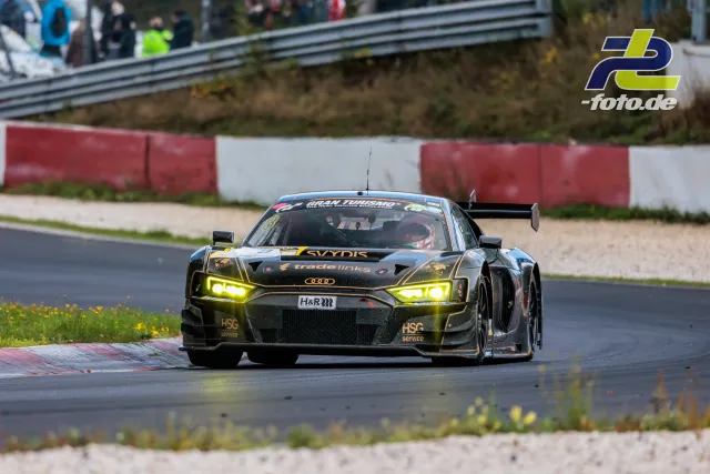 Schwarzer Audi R8 LMS GT3 mit gelben Details fährt auf dem Nürburgring am Kiesbett und rot-weißem Randstein vorbei.