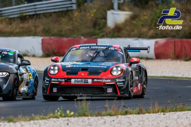 Ein rot-schwarzer Porsche 911 GT3 Cup mit Heckspoiler auf nasser Strecke, gefolgt von einem weiteren Fahrzeug auf dem Nürburgring.