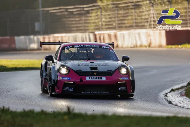 Porsche 911 GT3 Cup in weiß-violetter Lackierung fährt im Qualifying auf dem Nürburgring durch eine Kurve mit eingeschalteten Scheinwerfern.