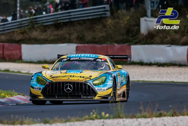 Mercedes-AMG GT3 in gelb-blauer Lackierung auf der Nürburgring-Nordschleife während des NLS-Rennens, Zuschauer im Hintergrund.