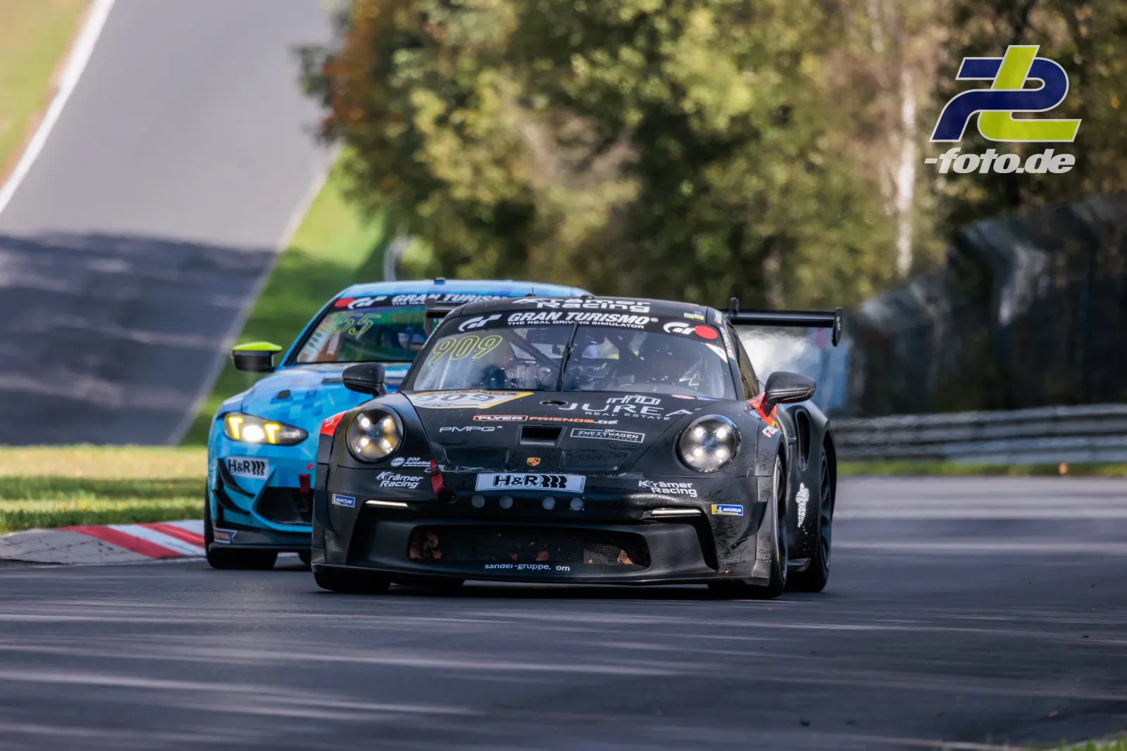 Schwarzer Porsche 911 GT3 Cup #909 von KKraemer Racing vor blauem Fahrzeug während des Rennens am Nürburgring bei der NLS Sportwarte-Trophy.