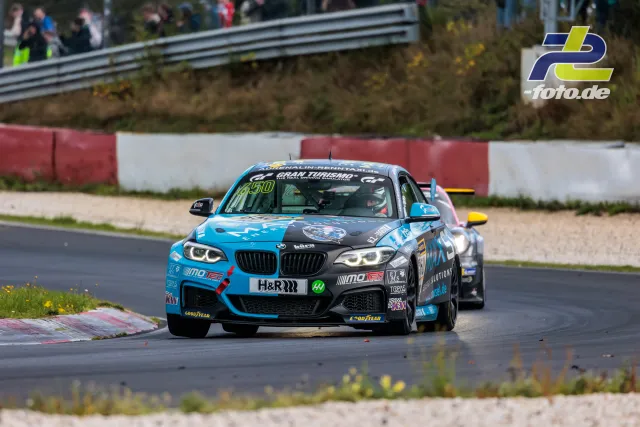 BMW M240i Nummer 650 in türkisblau-schwarzer Lackierung vor Verfolger in der Kurve auf dem Nürburgring bei der NLS Sportwarte-Trophy.