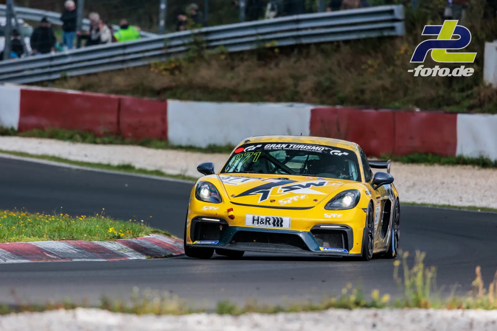 Gelber Porsche Cayman in Kurve auf der Nordschleife, Startnummer 950, H&R Sponsoring, Kiesbett und rot-weiße Randsteine