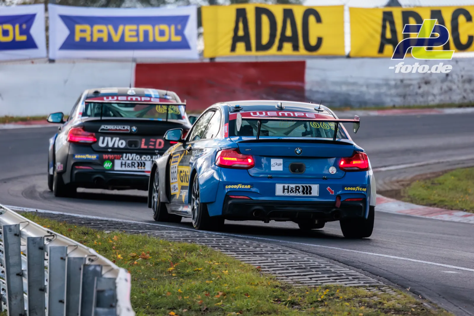 Zwei Rennwagen im Zweikampf auf dem Nürburgring bei der NLS Sportwarte-Trophy, Heckansicht mit leuchtenden Bremslichtern.