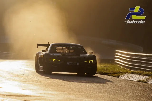 Rennwagen im Gegenlicht auf der Nordschleife, gelbe Tagfahrlichter leuchten, Leitplanke am Streckenrand