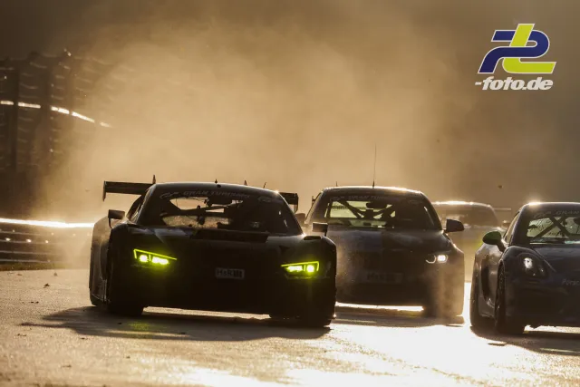 Rennwagen im Gegenlicht auf dem Nürburgring beim Qualifying, vorne ein GT-Fahrzeug mit gelben Scheinwerfern im Dunst