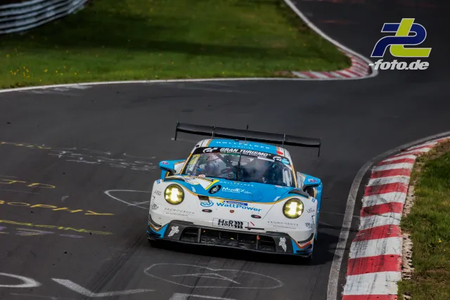 Porsche 911 GT3 R in blau-weißer Lackierung mit Gran Turismo-Sponsoring in einer Kurve auf der Nordschleife am Nürburgring