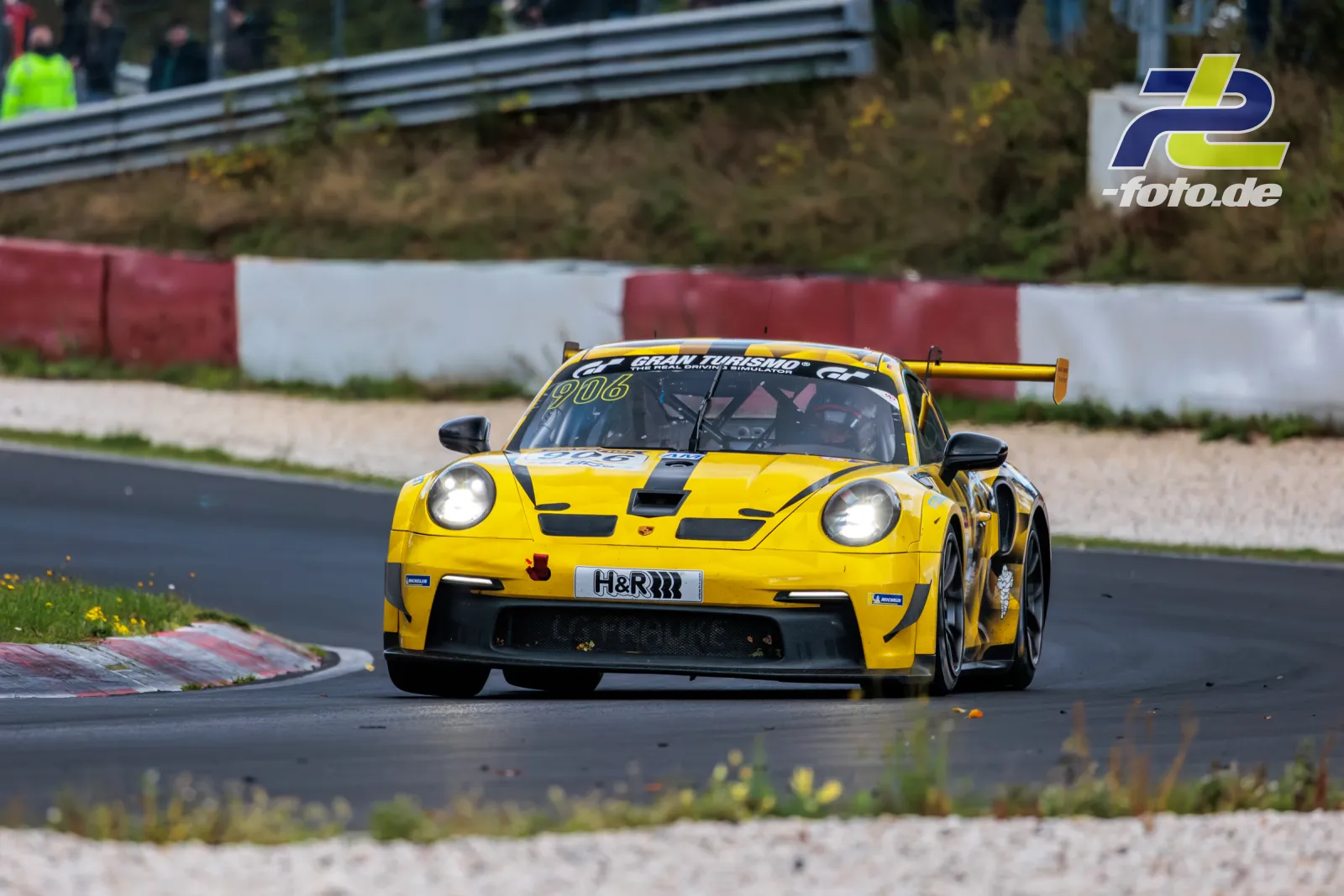 Gelber Porsche 911 GT3 Cup Nr. 906 in der Kurve beim NLS-Rennen auf dem Nürburgring, frontale Perspektive mit Kiesbett.