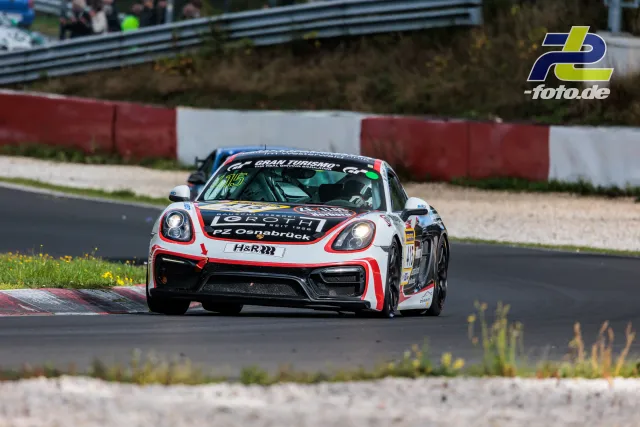 Porsche 718 Cayman GT4 #415 in weiß-roter Lackierung fährt durch eine Kurve auf der Nordschleife beim NLS-Rennen.