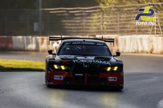 BMW M4 GT3 in schwarz-roter Yokohama-Lackierung während des Qualifyings auf dem Nürburgring, Frontansicht mit eingeschalteten Scheinwerfern.