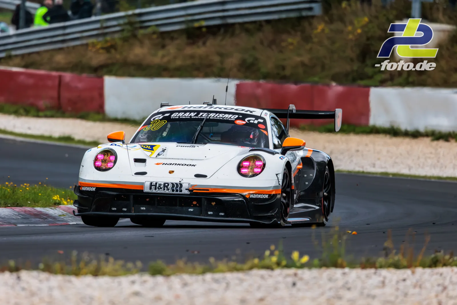 Weißer Porsche 911 GT3 R mit orangenen Akzenten auf der Nordschleife während des Rennens, Startnummer 30