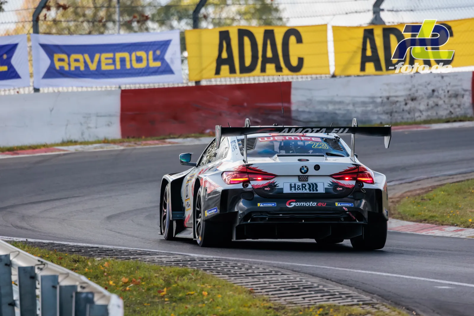 BMW M4 GT3 EVO von Gamota Racing auf der Nürburgring-Nordschleife bei der NLS, Heckansicht mit leuchtendem Rücklicht während des Rennens.