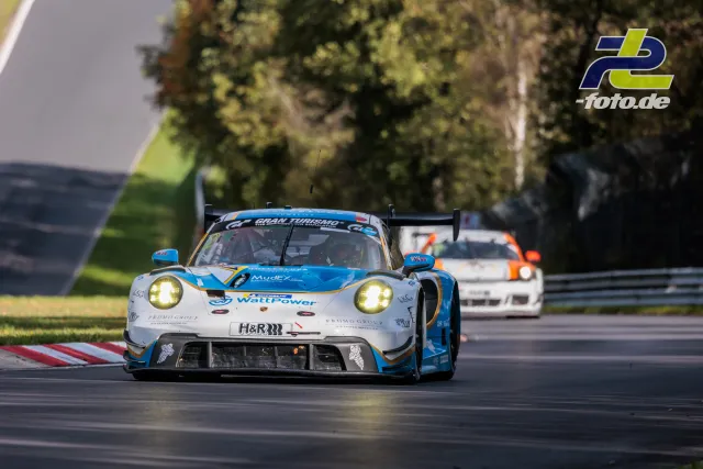 Porsche GT3-Rennauto mit blau-weißer Lackierung auf der Nürburgring-Nordschleife, gefolgt von einem Konkurrenten.