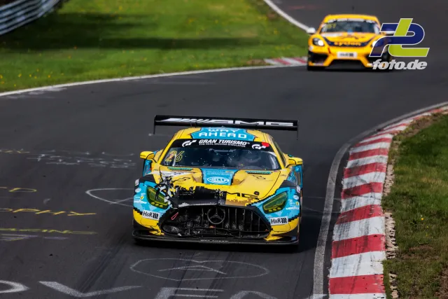 Mercedes-AMG GT3 in gelb-blauer Lackierung führt auf der Nordschleife vor einem Porsche Cayman. Frontalperspektive in einer Kurve.