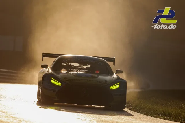 GT3-Rennwagen mit neongelben Scheinwerfern fährt im Gegenlicht durch Staubwolke auf der Nürburgring-Nordschleife.