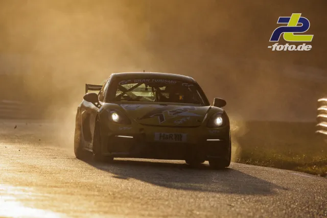 Porsche Cayman GT4 von Avia Sorg fährt bei tiefstehender Sonne durch eine staubige Kurve am Nürburgring während des Qualifyings.