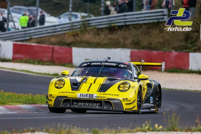 Gelb-schwarzer Porsche 911 GT3 R in Kurvenfahrt am Nürburgring, Zuschauer hinter der Leitplanke, NLS Sportwarte-Trophy.