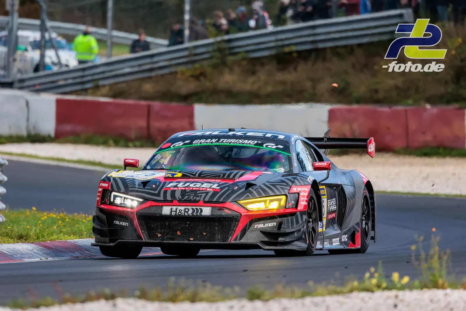 Audi R8 LMS GT3 in schwarz-roter Zebra-Lackierung während des Rennens auf dem Nürburgring, Zuschauer im Hintergrund.