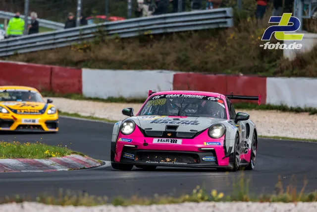 Pink-weißer Porsche 911 GT3 Cup in Kurve auf der Nordschleife, gefolgt von gelbem Fahrzeug. Zuschauer hinter Leitplanke.