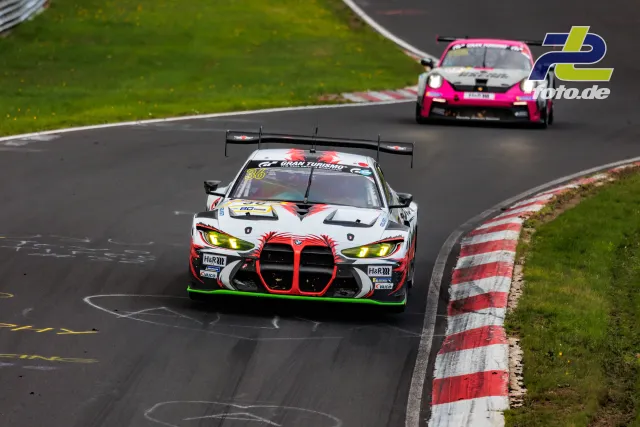BMW M4 GT3 mit markanter Nieren-Grafik führt vor pinkem Porsche durch Nordschleifen-Kurve auf dem Nürburgring.