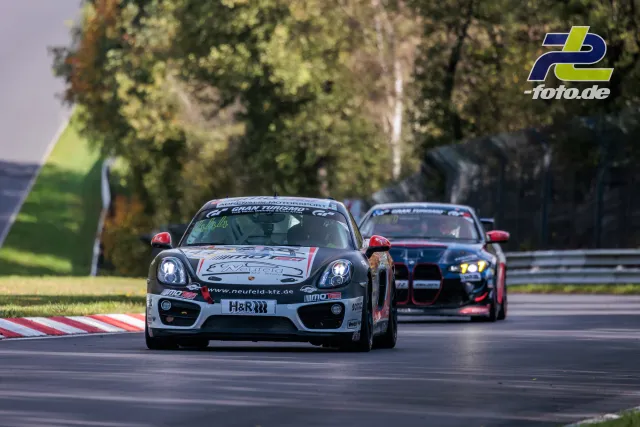 Porsche Cayman führt vor Verfolger durch Kurve beim NLS-Rennen auf dem Nürburgring, Randstein im Vordergrund.