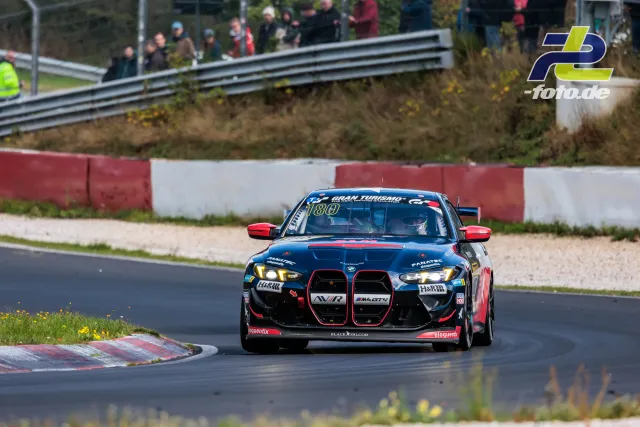 BMW M4 GT4 Nummer 180 in dunkelblau-roter Lackierung auf der Nordschleife beim NLS-Rennen vor Zuschauern.
