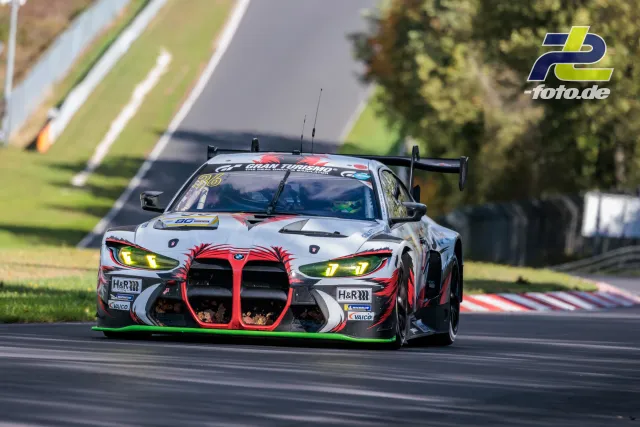 BMW M4 GT3 mit rot-weißer Lackierung und grünem Unterboden während des NLS-Rennens auf dem Nürburgring.
