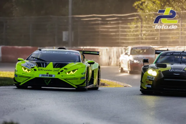 Drei Rennwagen beim Qualifying auf dem Nürburgring, neongrüner Lamborghini und Aston Martin in Verfolgungsduell bei Gegenlicht.