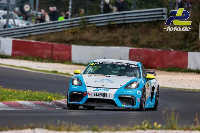 Porsche 718 Cayman GT4 in blau-weißer Lackierung mit Startnummer 977 in Kurve auf der Nürburgring-Nordschleife beim NLS-Rennen.