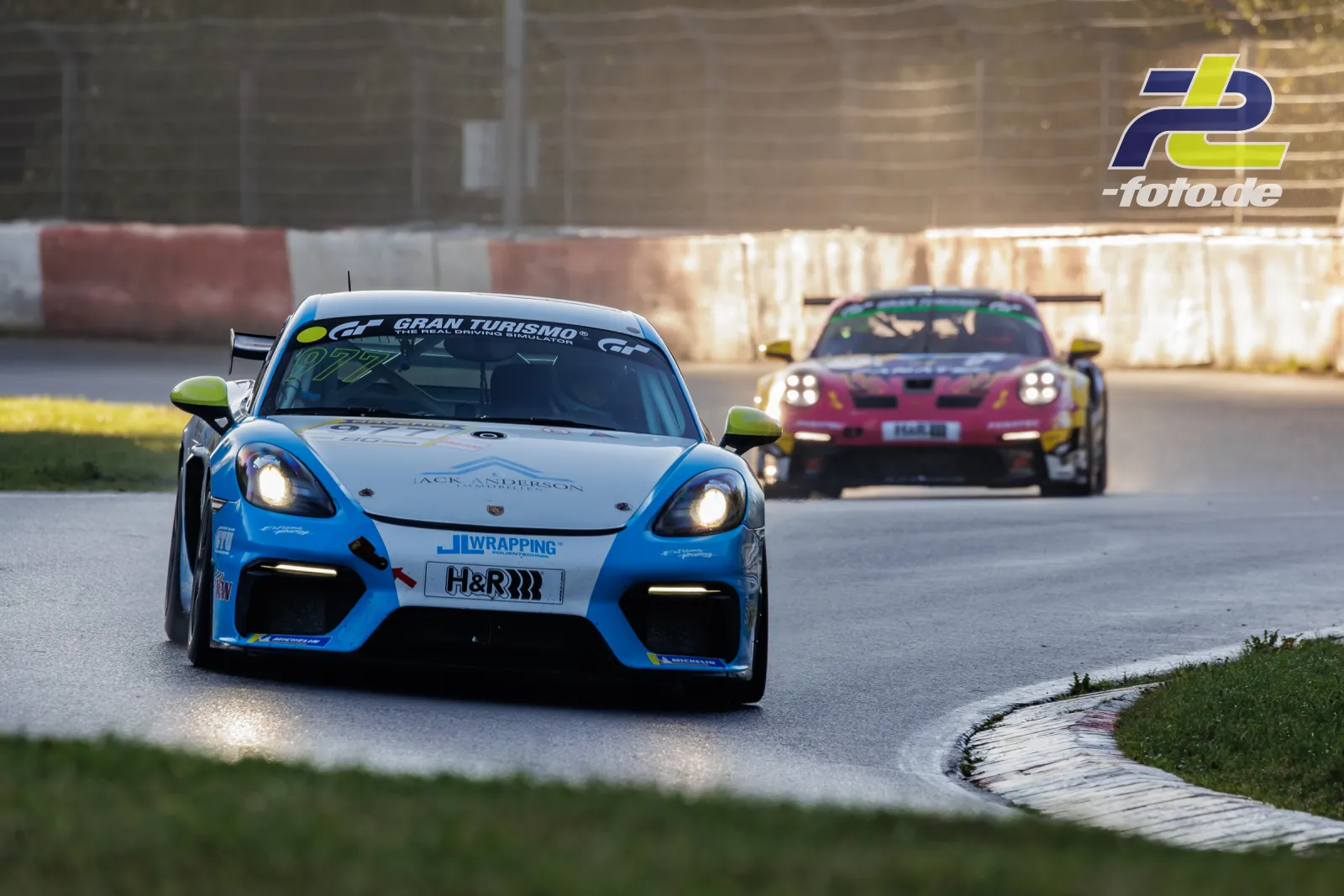 Zwei Porsche-Rennwagen in einer Kurve beim NLS-Qualifying auf dem Nürburgring, weißer 718 Cayman GT4 vor pinkem 911 GT3.