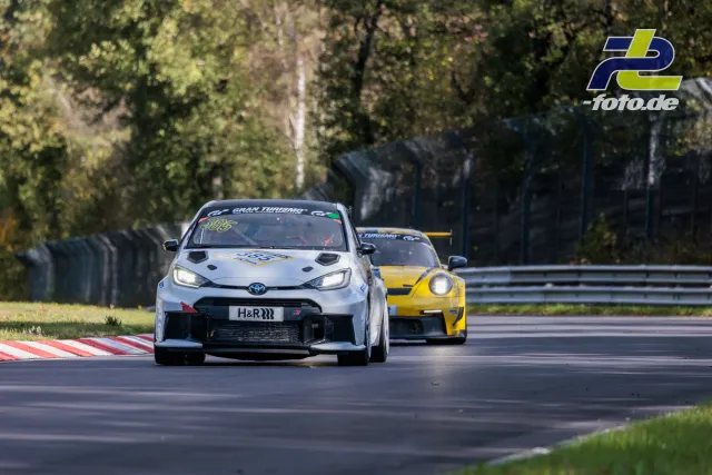 Weißer Toyota GR führt vor gelbem Porsche GT3 durch Kurve auf der Nordschleife bei sonnigem Herbstwetter.