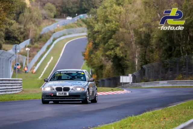 Silberner BMW E46 auf der Nürburgring-Nordschleife während der NLS Sportwarte-Trophy im Herbst, umgeben von herbstlichem Wald.