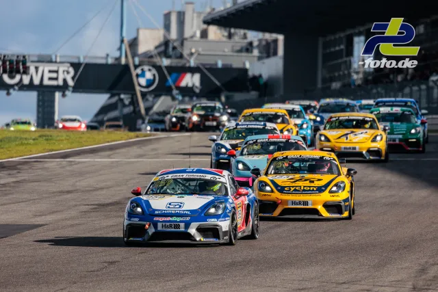 Starterfeld bei der Einführungsrunde auf dem Nürburgring, angeführt von Porsche Cayman GT4 Clubsport in blau-weiß-roter Lackierung.