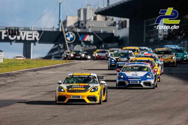 Einführungsrunde NLS am Nürburgring: Porsche Cayman GT4 führt das Feld auf der Geraden an, BMW M Brücke im Hintergrund.