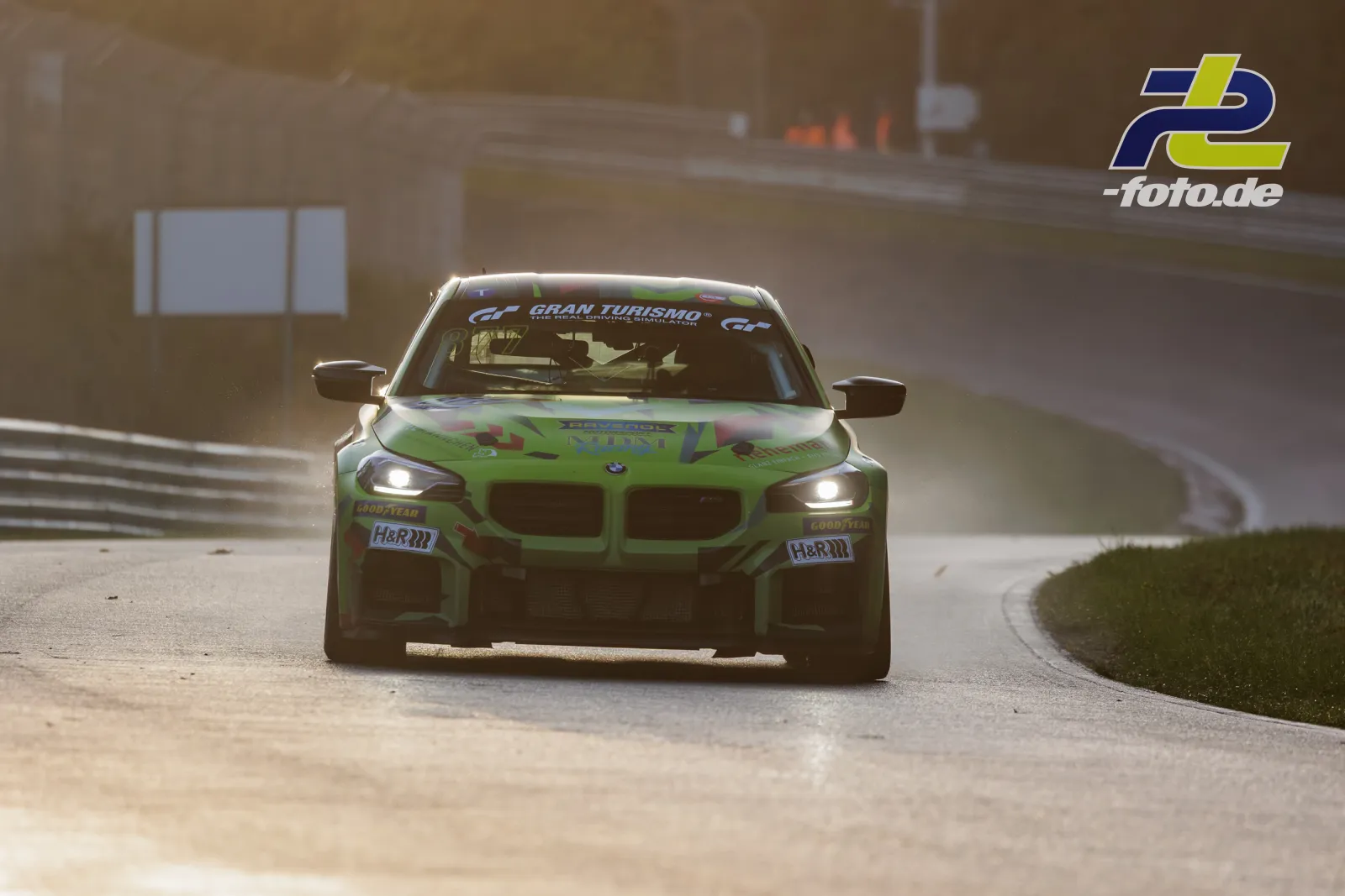 BMW M4 GT3 in auffälliger grüner Lackierung frontal auf Nordschleife bei Gegenlicht mit eingeschaltetem Licht.