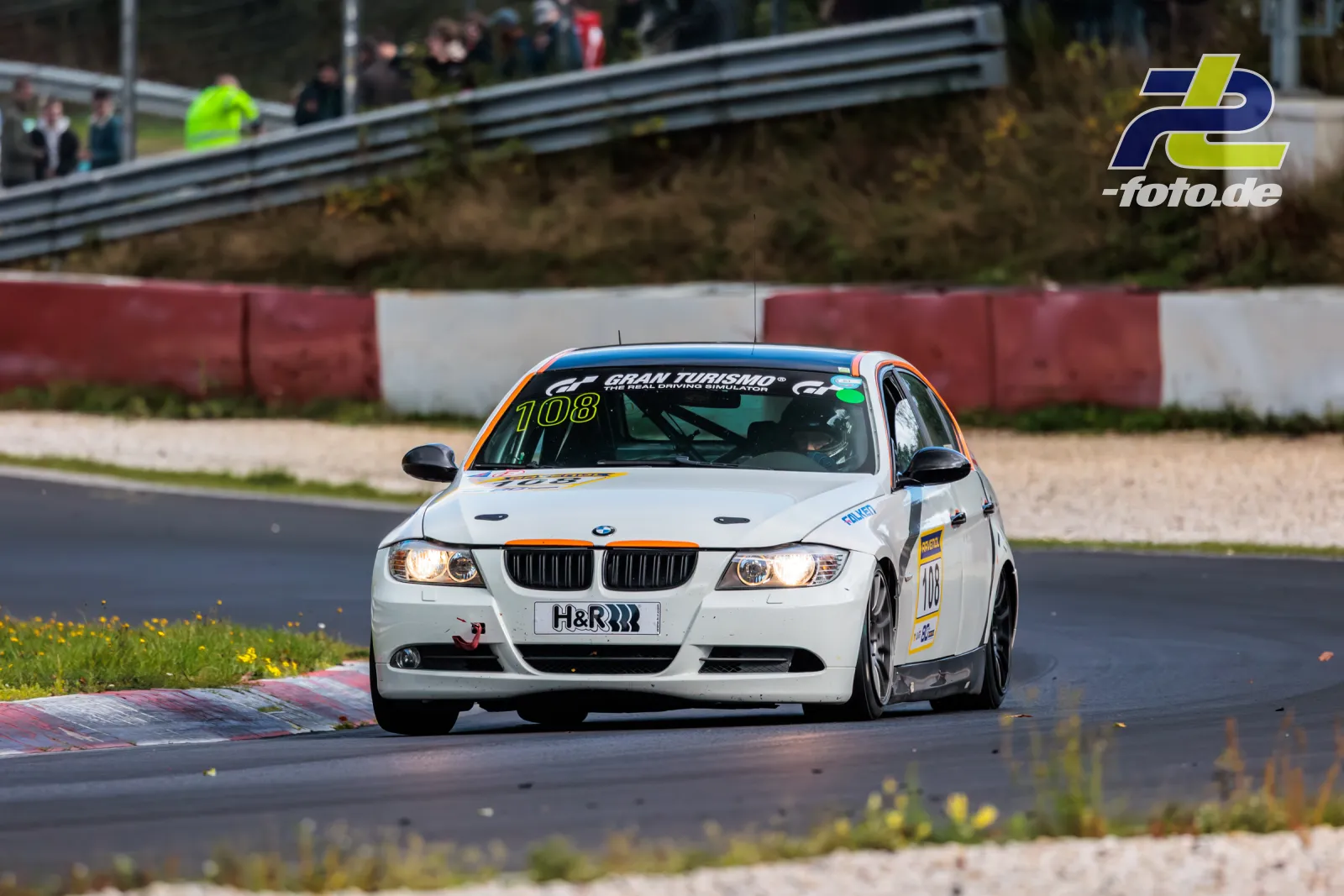 Weißer BMW 325i in Kurve auf dem Nürburgring, im Hintergrund Zuschauer und Leitplanken, NLS Lauf 10