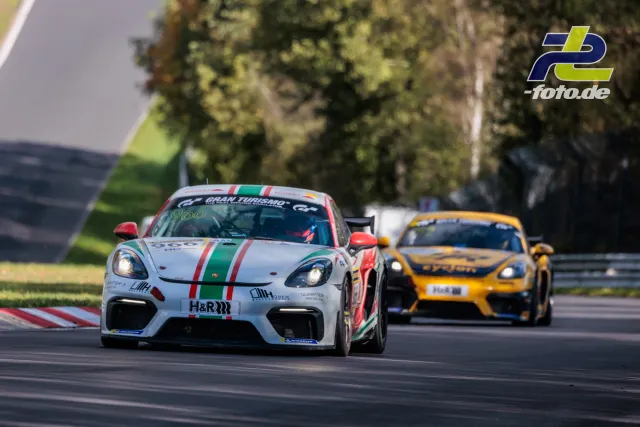 Zwei Porsche Cayman GT4 auf der Nordschleife, weißer #966 vor gelbem Verfolger, Grünstreifen und Bäume im Hintergrund.