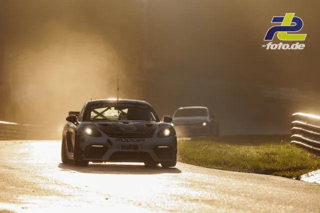 Porsche Cayman GT4 CS im Gegenlicht auf der Nordschleife während des Qualifyings, gefolgt von einem weiteren Rennwagen.
