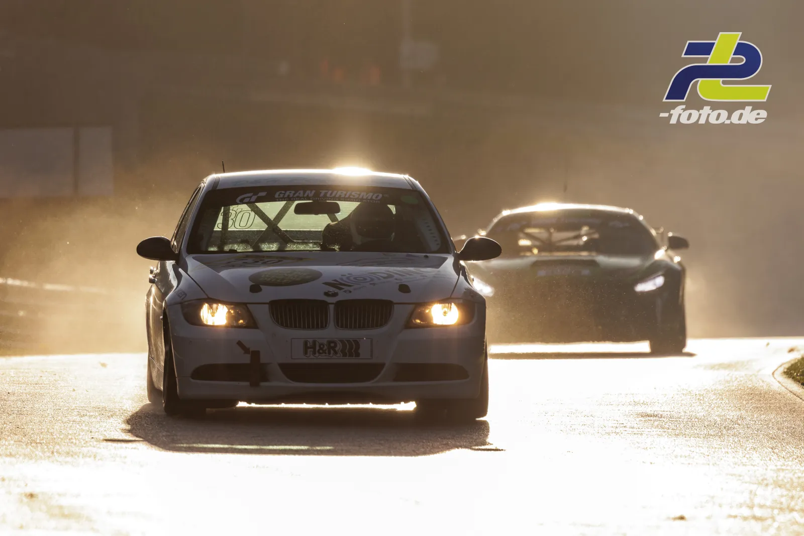 Zwei Rennwagen im Gegenlicht bei staubigen Bedingungen auf dem Nürburgring während der NLS Sportwarte-Trophy.