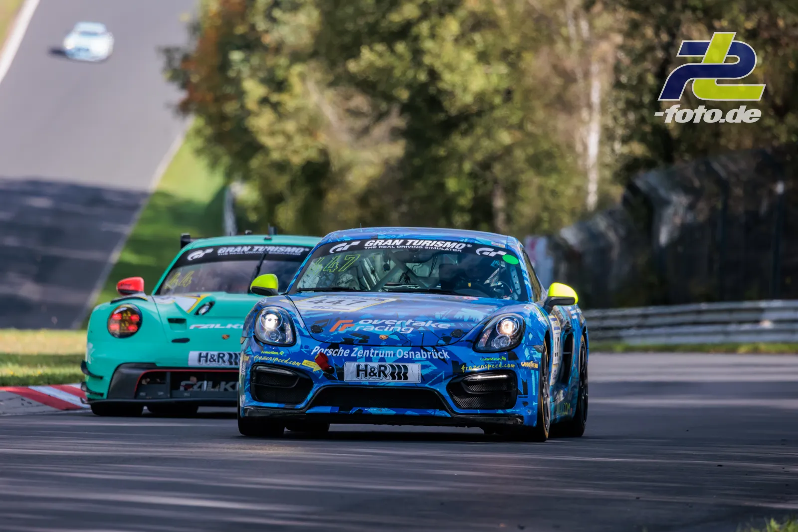 Zwei Porsche Cayman während des Rennens auf dem Nürburgring, vorne ein blau lackierter Wagen mit Werbung für Porsche Zentrum Osnabrück.